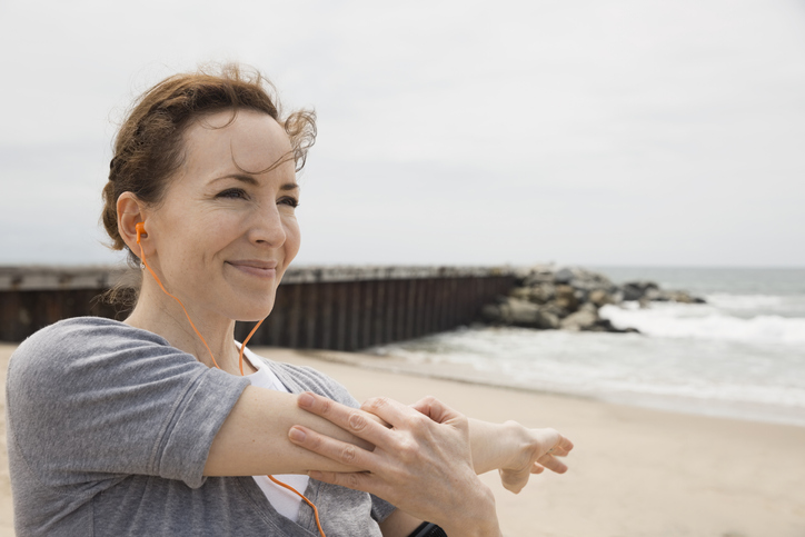 A woman stretches her arm before jogging on a beach - New Year's Resolutions